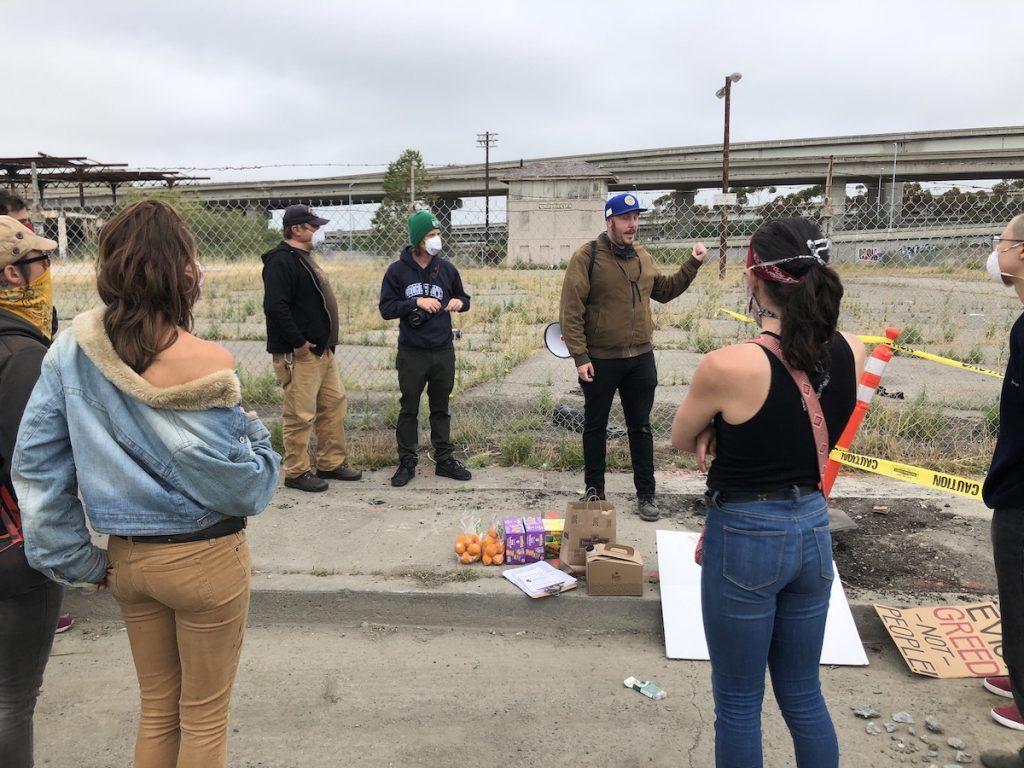 A group of people stand in a circle outside, with the freeway in the background