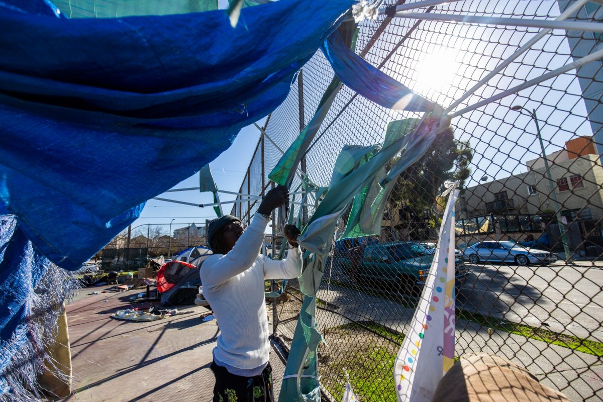 man pulls pieces of fabric off a fence. A tarp hangs overhead