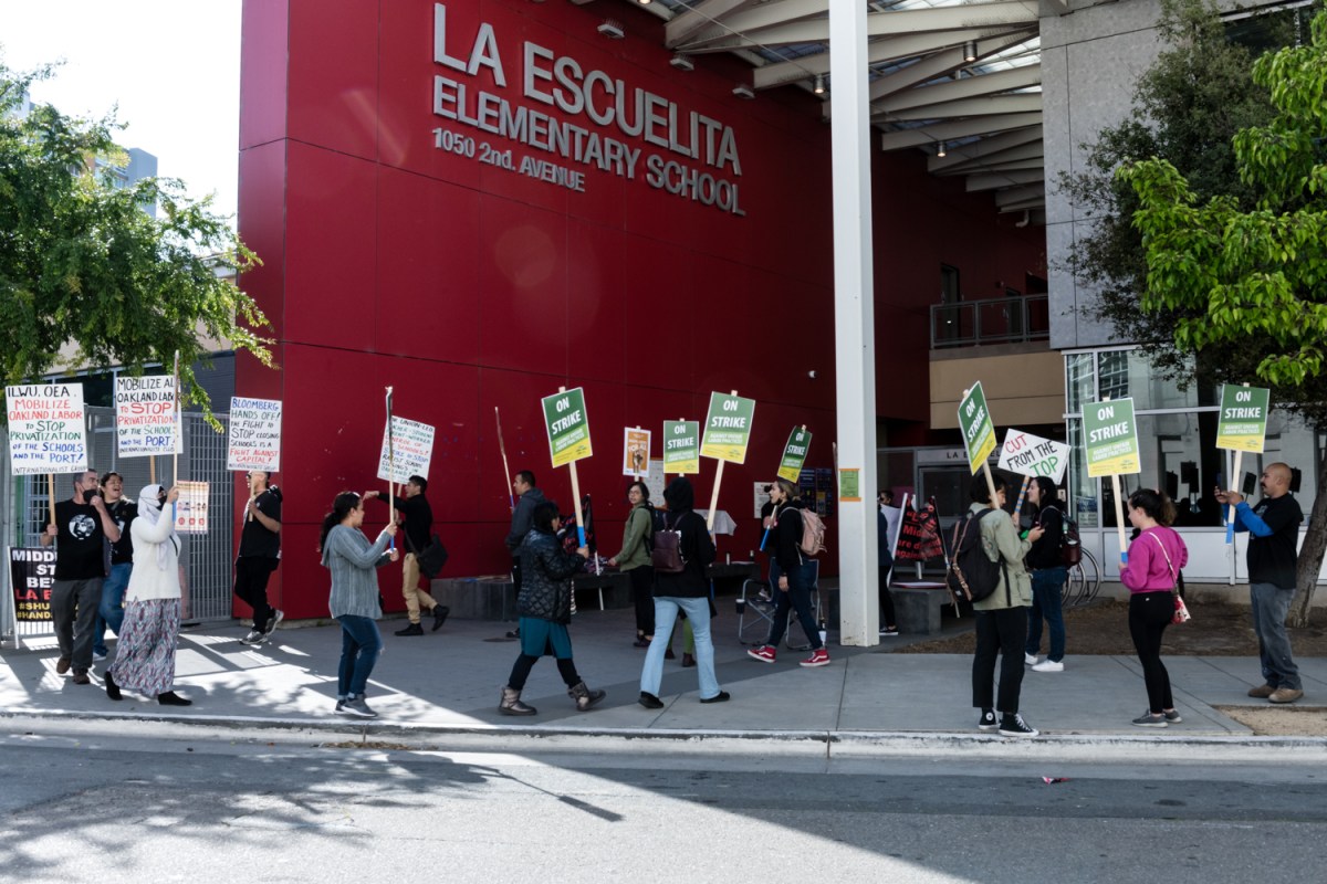 Oakland teachers and supporters march in front of La Escuelita Elementary School holding signs that they are on strike.
