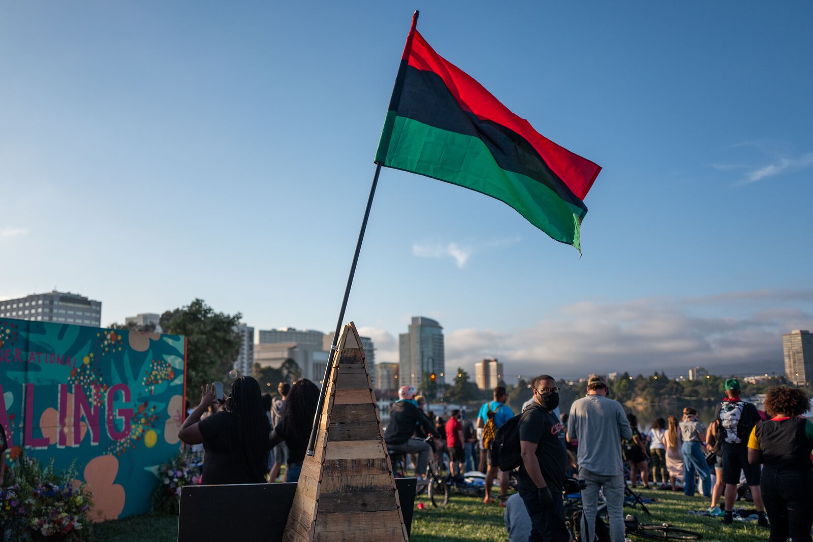 A pan-African flag stands tall above a crowd of people gathered with buildings in the background