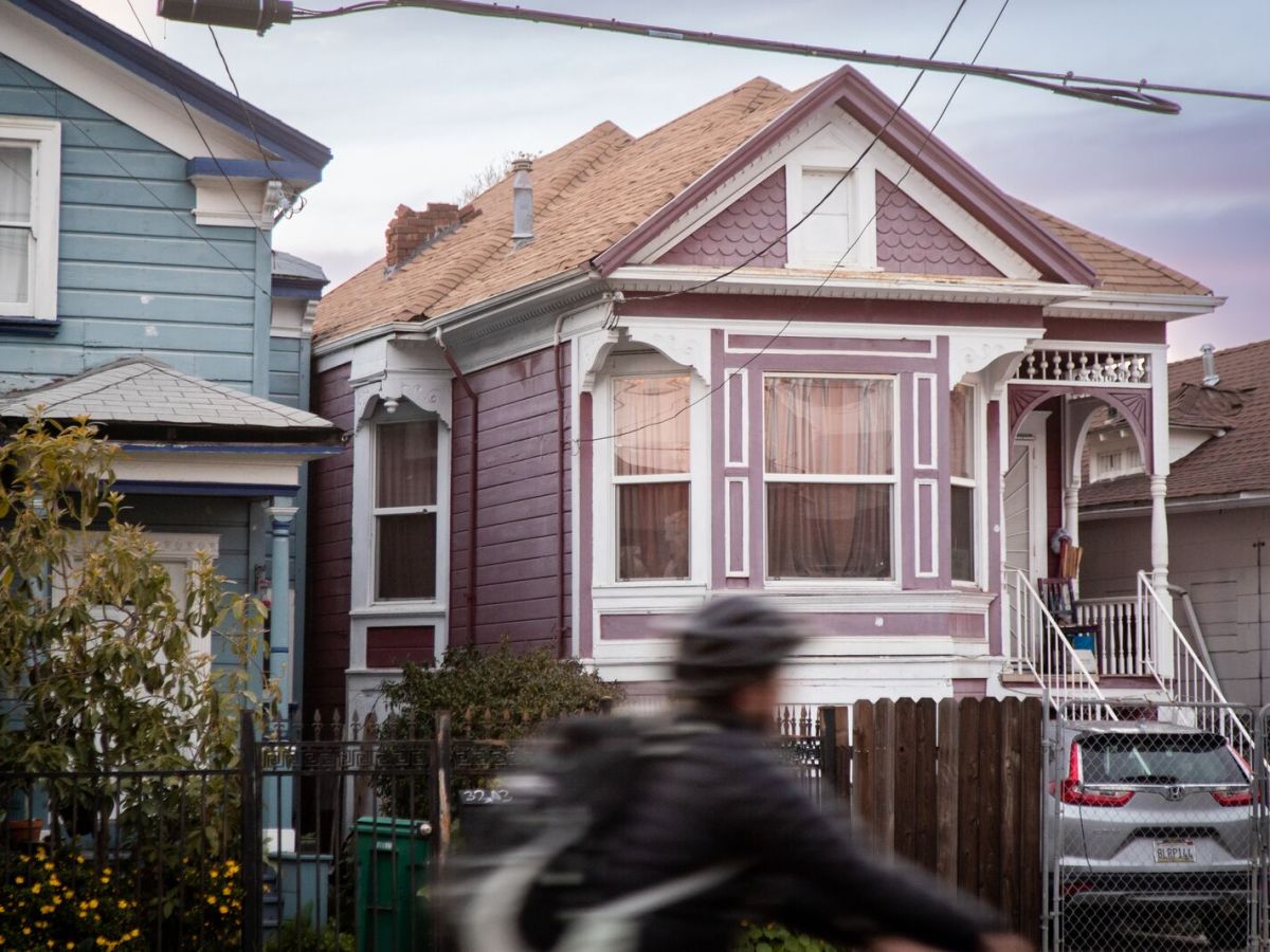Woman in helmet rides a bike, in a blur, past victorian houses.