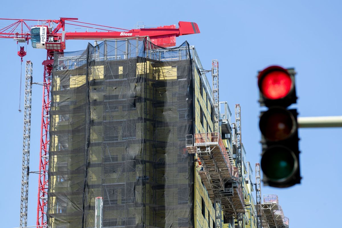 Image of a large under-construction building with a crane over it. A red traffic light is in the foreground.