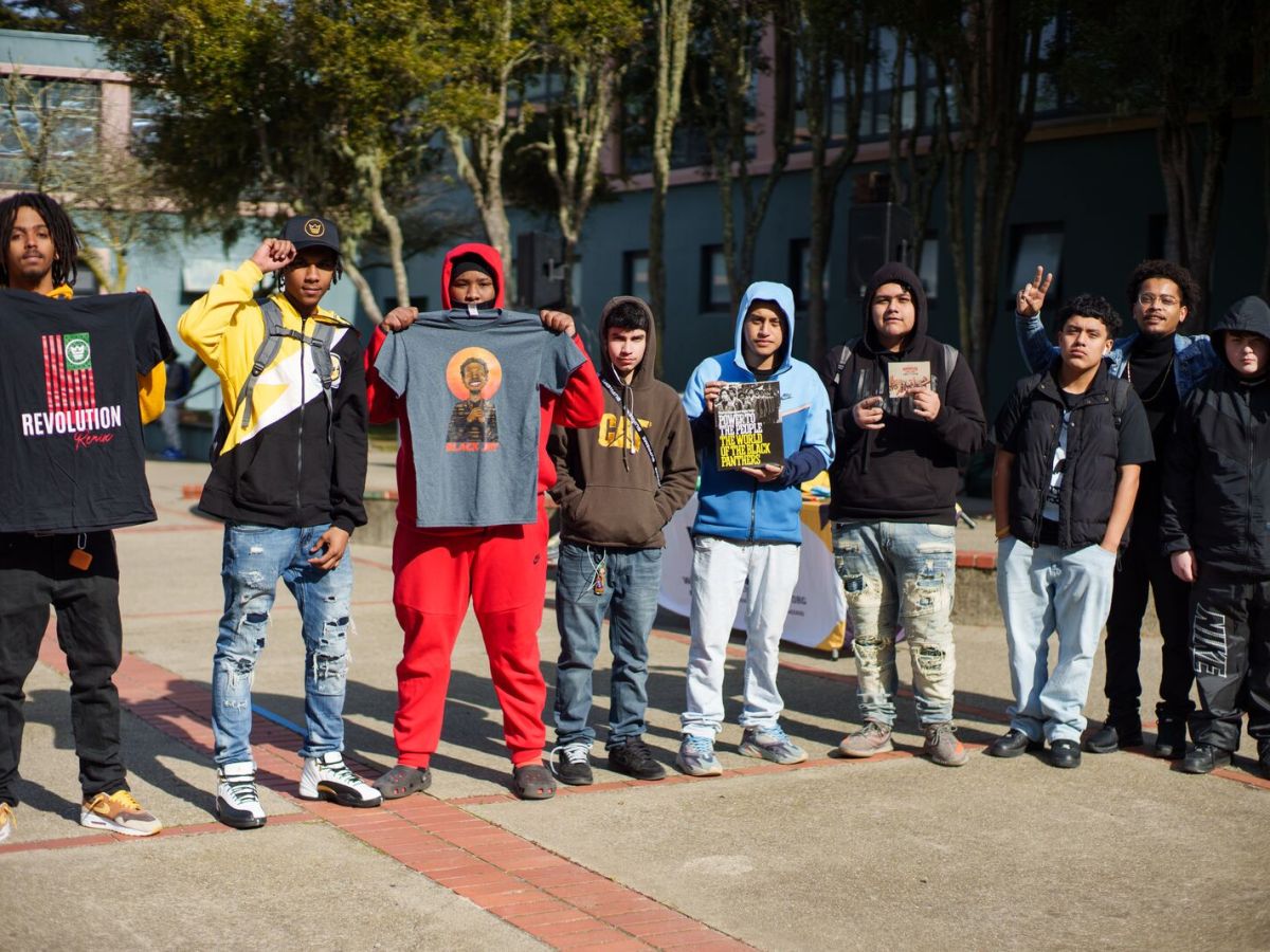 boys of color line up showing off t-shirts in the courtyard of a school