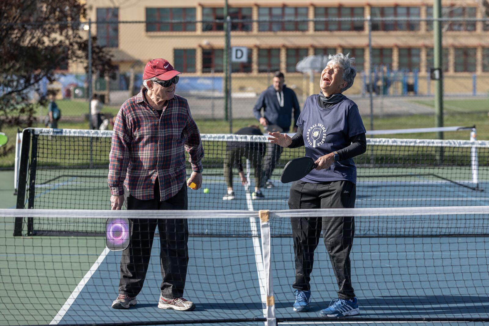 Two people stand smiling and laughing on a pickleball court.