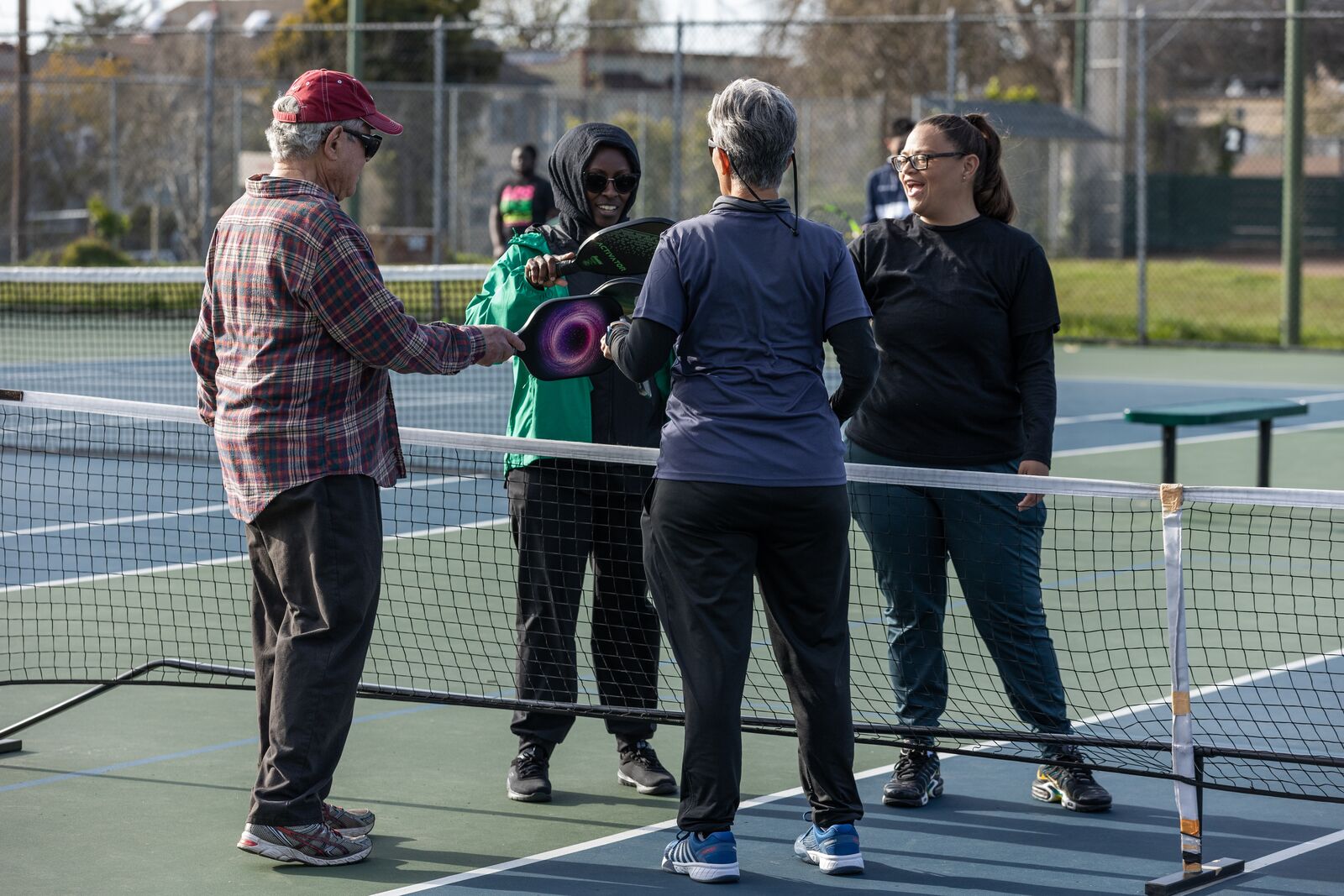 Four people tapping paddles over the net at the center of a court.