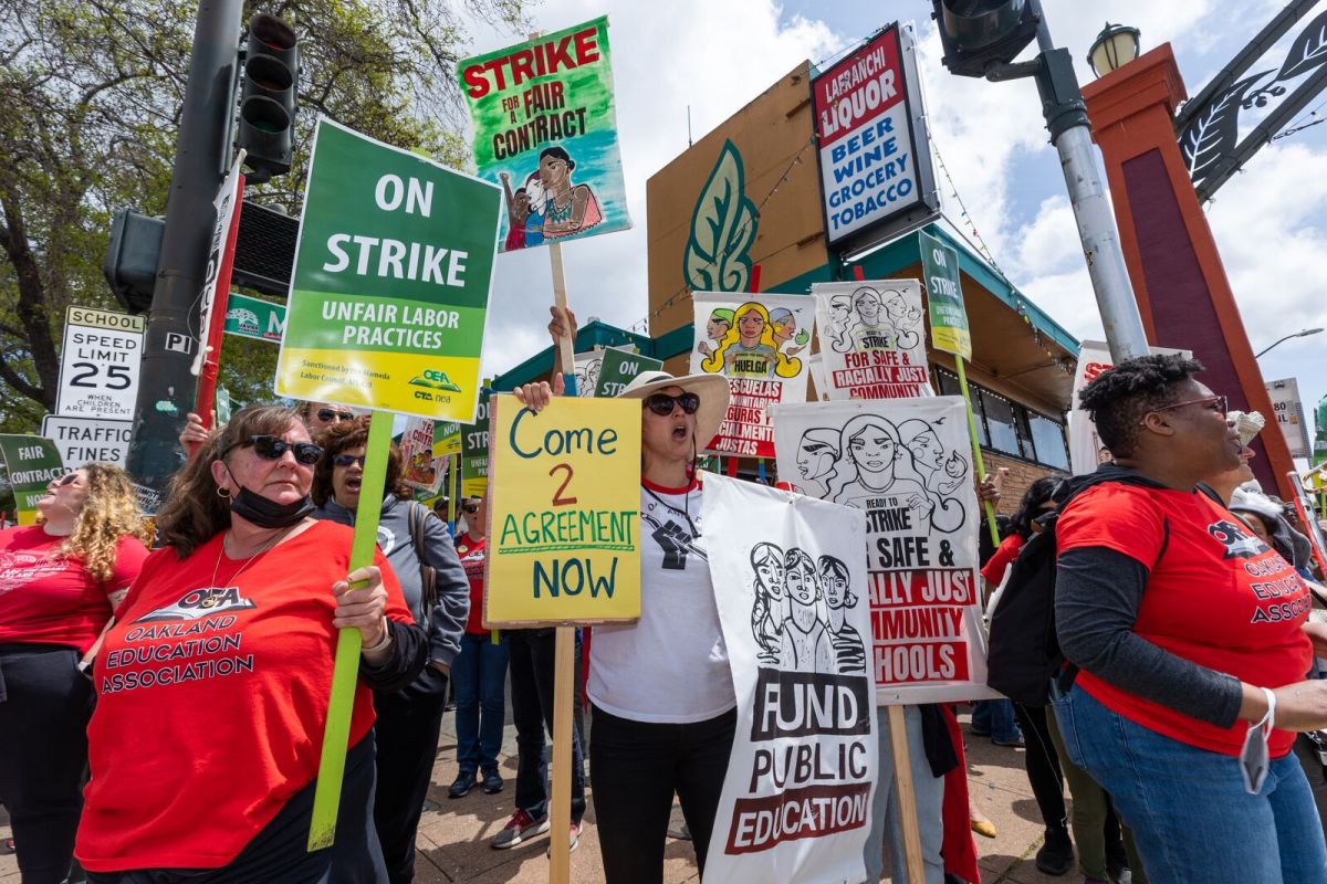 Oakland teachers and supporters hold signs that say "on strike!" and "come 2 agreement now" on a picket line near 35th Avenue and MacArthur Boulevard in Oakland