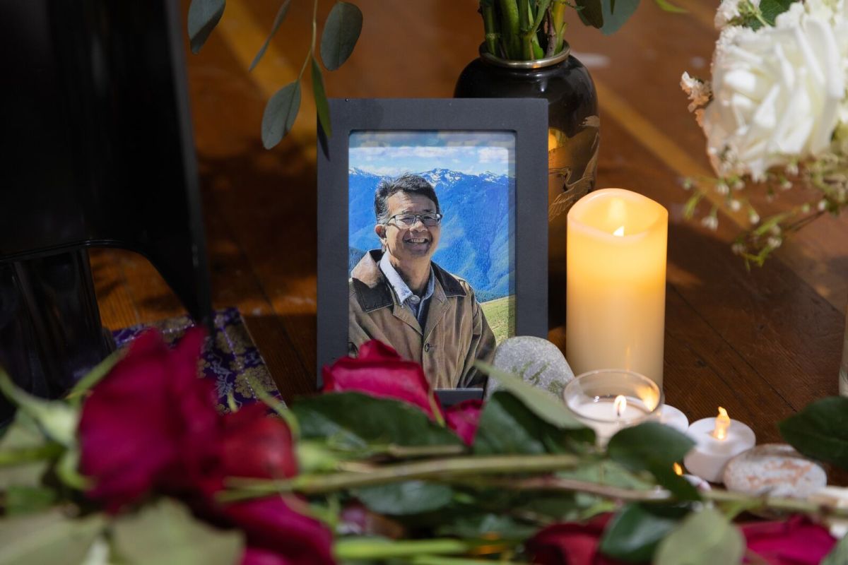 A framed photo of David Sakurai sits next to a lit candle, with roses laying in front on an altar
