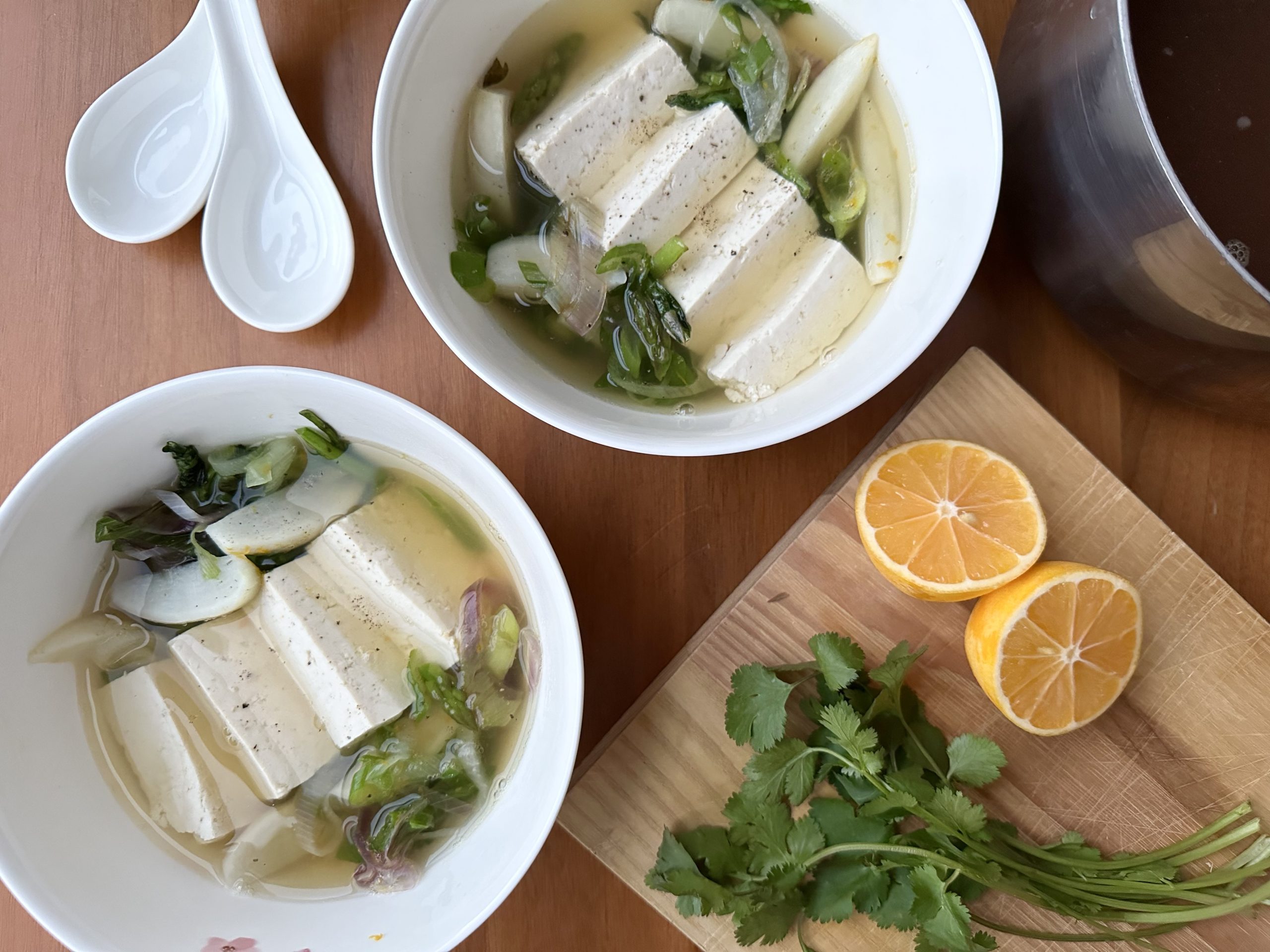 Two white bowls of tofu, vegetable and broth soup