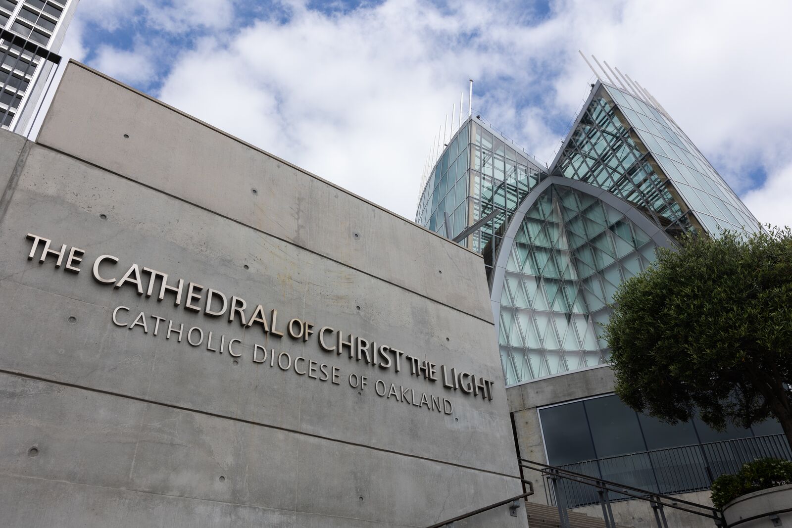 A gleaming cathedral made up entirely of steel and glass rises above a cement wall with a neat metal lettered sign that reads "The Cathedral of Christ the Light," and "Diocese of Oakland."