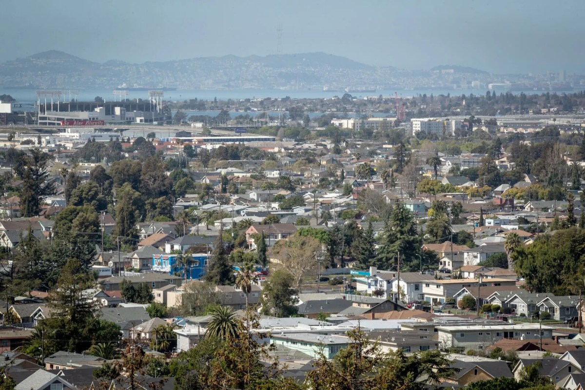 A panaoramic view of homes in residential neighborhoods. In the distance there is the Oakland Coliseum and bay.