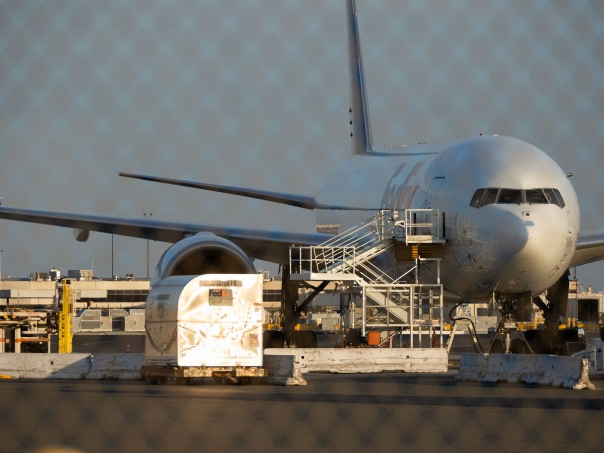 A FedEx cargo plane is parked near a terminal with a ramp propped against the cockpit. There are concrete barriers arrayed near the plane.
