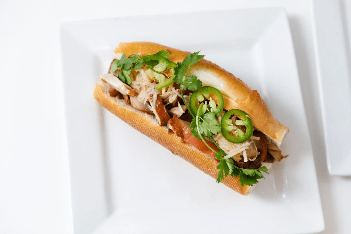 A bahn mi sandwich on a white plate on top of a white table.