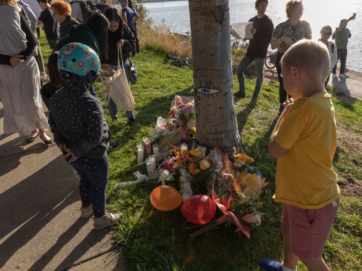 Two children stand over a bundle of flowers and a picture of Maia Correia near Lake Merritt.