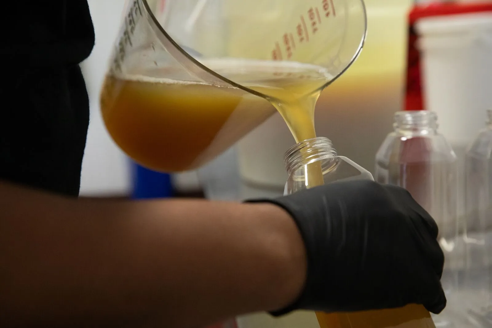 Closeup of a someone's hands pouring a large measuring cup of golden liquid into a glass bottle.
