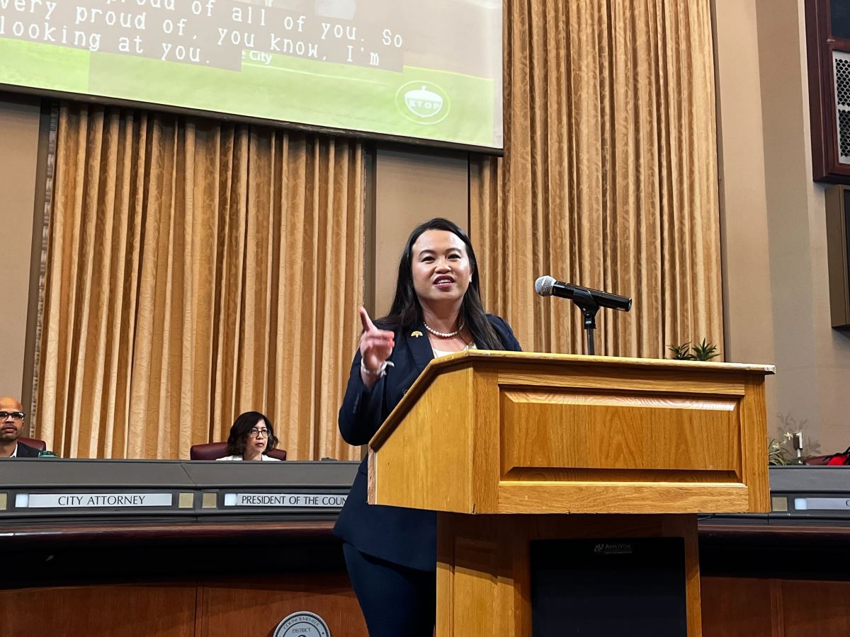 Oakland Mayor Sheng Thao speaking and pointing behind a podium in the council chamber.