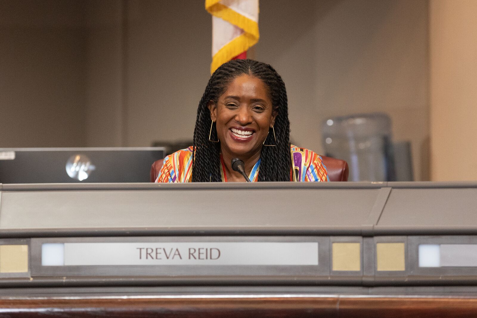 Councilmember Treva Reid smiling and sitting behind the dais of the city council chamber.