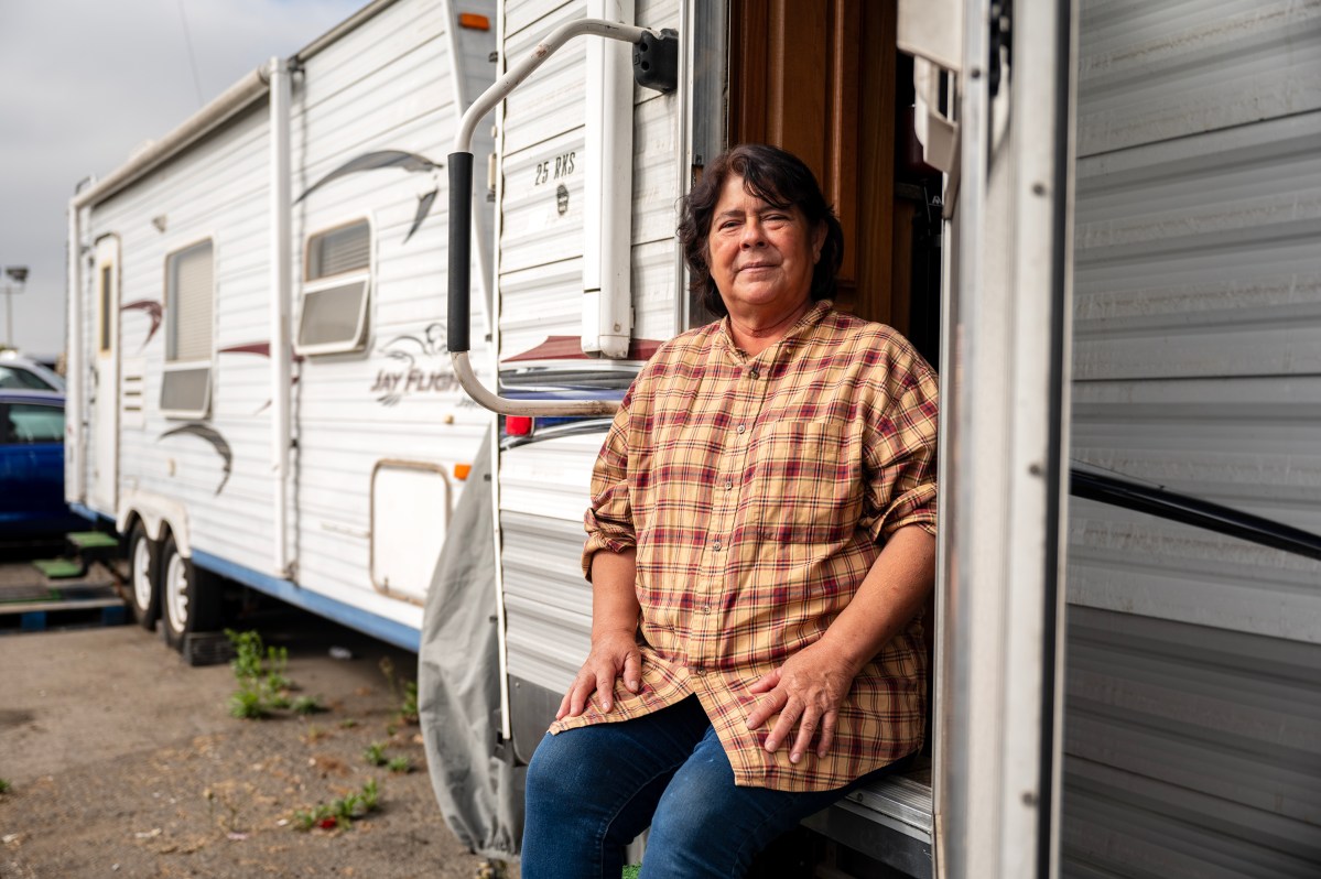 A Latina woman sits on the steps of a trailer home.