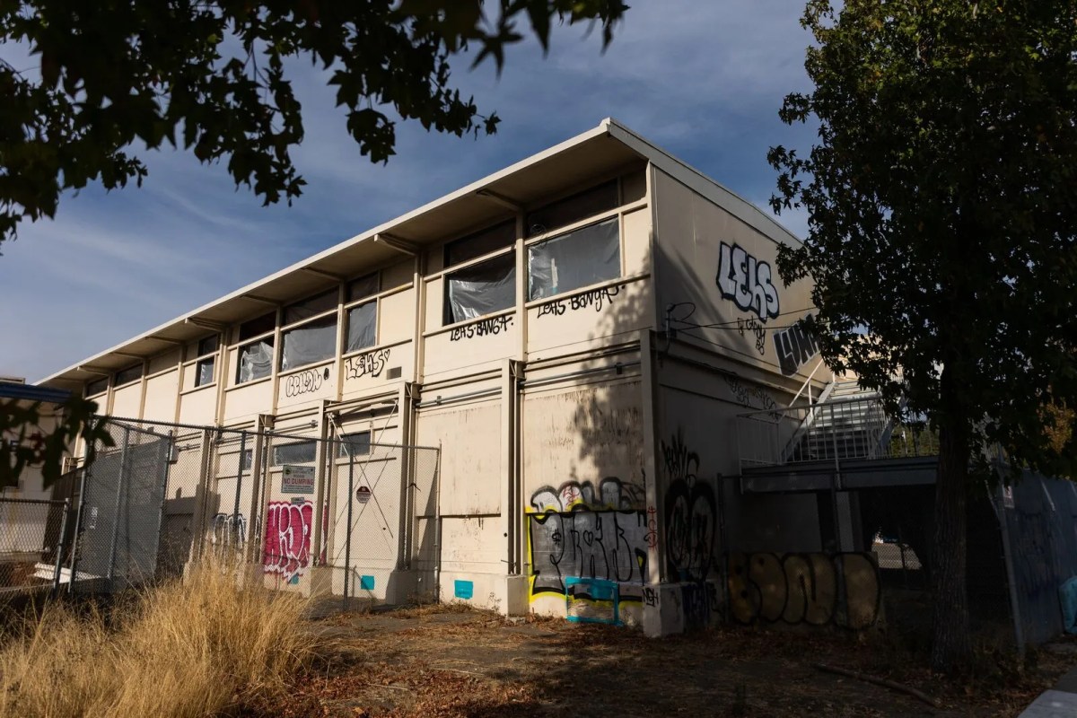 An old Oakland Unified School District building, its windows broken, graffiti on the walls.