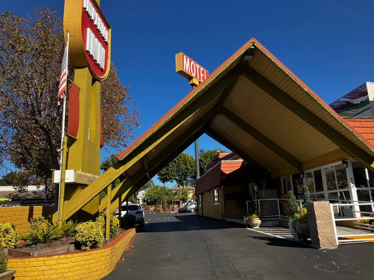 Goofy-looking motel with a pointy roof and a yellow sign sticking into the air.