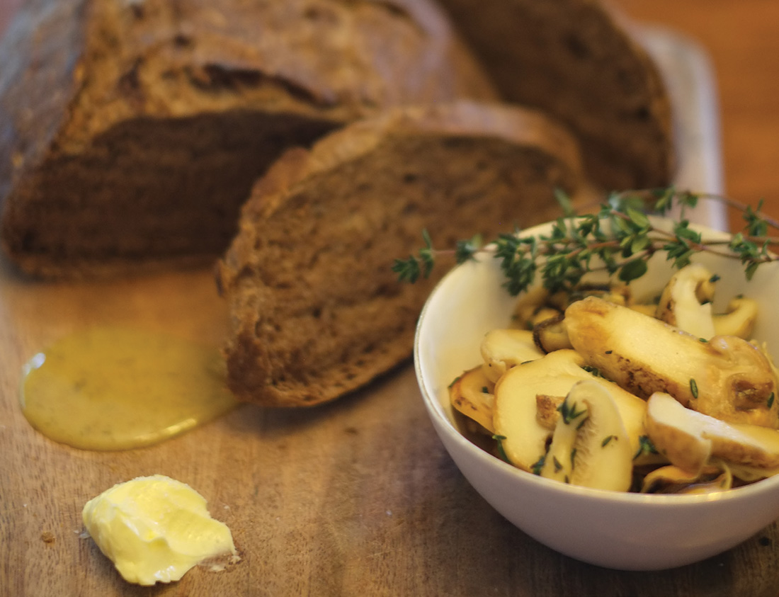 Sliced acorn bread served with butter and a bowl of mushrooms.