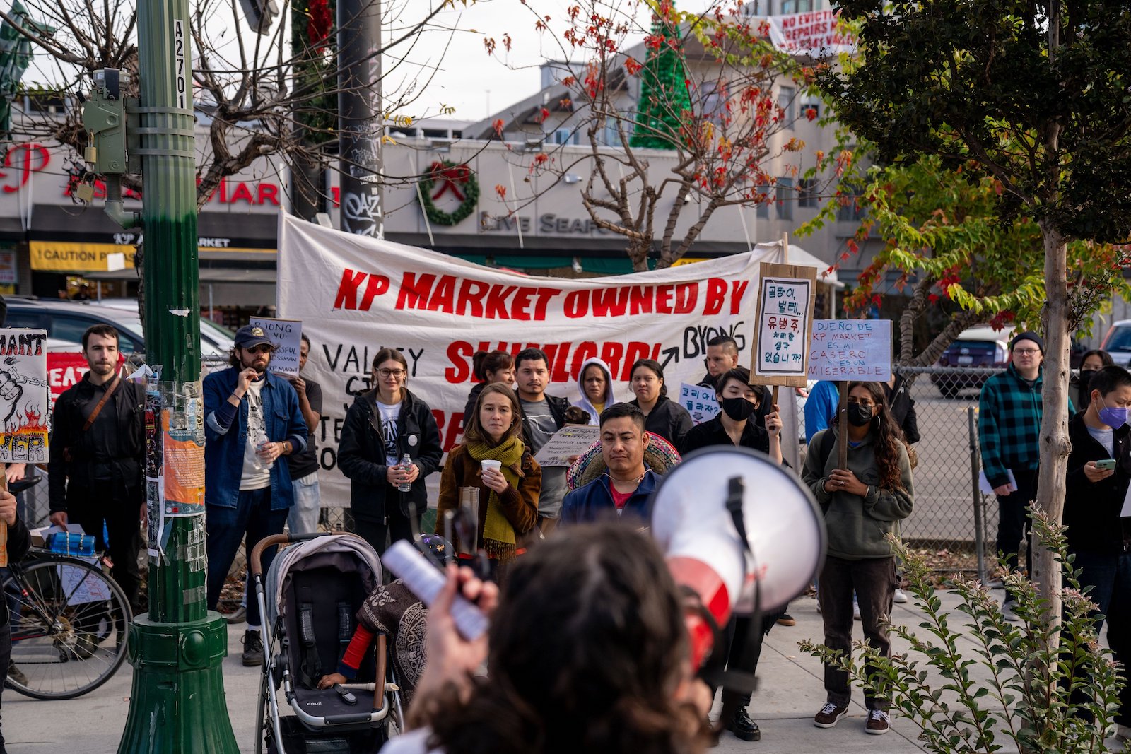 About 15 people protesting with a megaphone and a banner that says "KP Market owned by slumlord"
