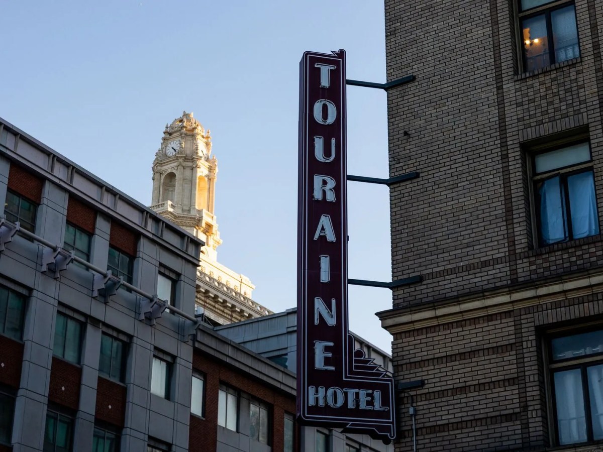 An old building with a sign that says "Touraine Hotel," with Oakland City Hall in the distance.