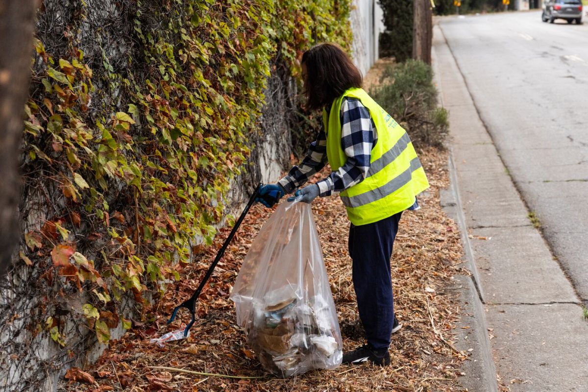 A woman in a flannel and high visibility vest cleans up trash on the road