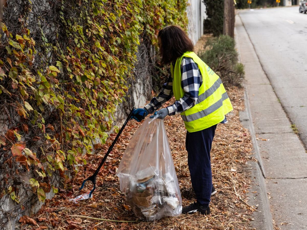 A woman in a flannel and high visibility vest cleans up trash on the road