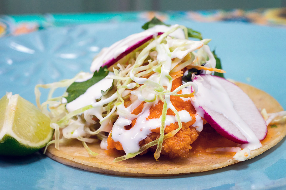 A fish taco from Cholita Linda, with a fried piece of fish on a tortilla with cabbage, radish, cilantro and crema.