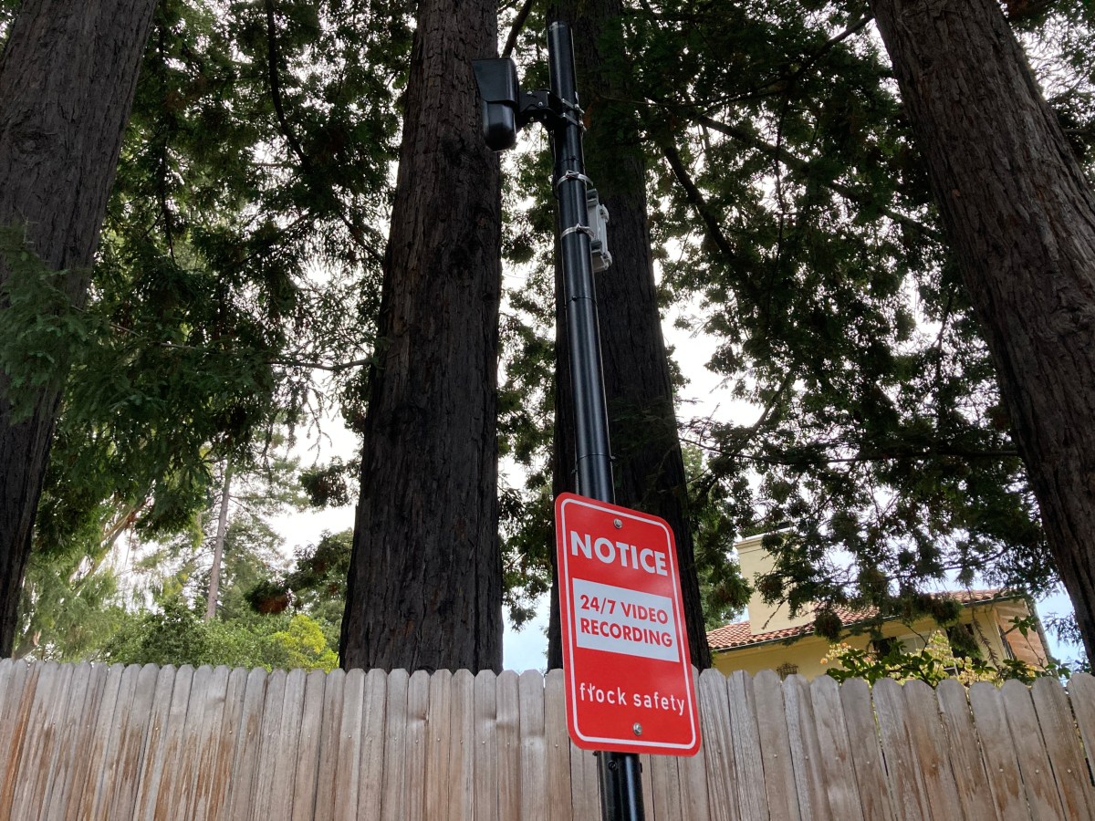 A red sign on a pole with a camera notifying passersby that they are being recorded.