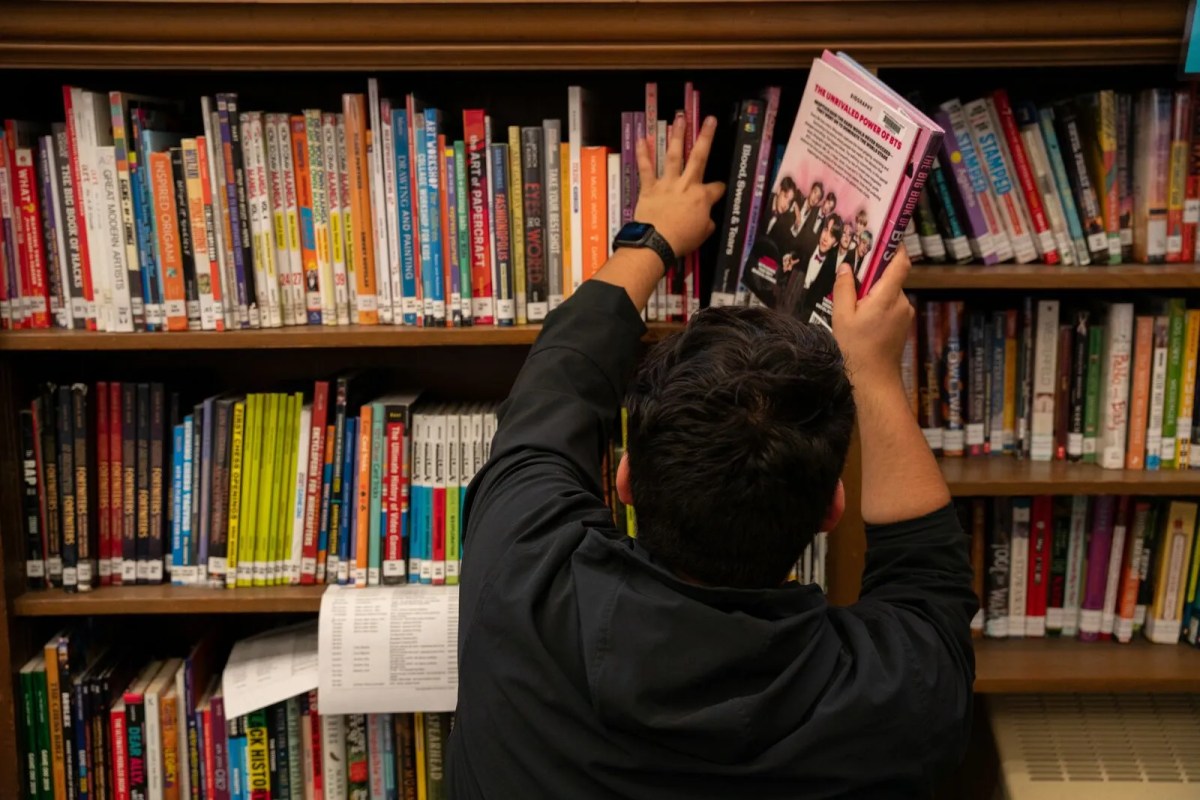 A teenager grabs a book off a bookshelf.