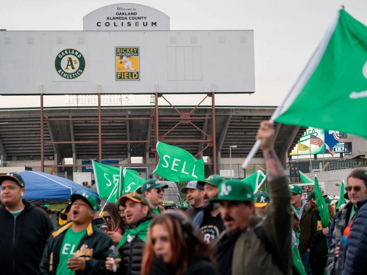 Fans decked out in A's gear wave flags with the word "sell" on them outside of the Oakland Coliseum.