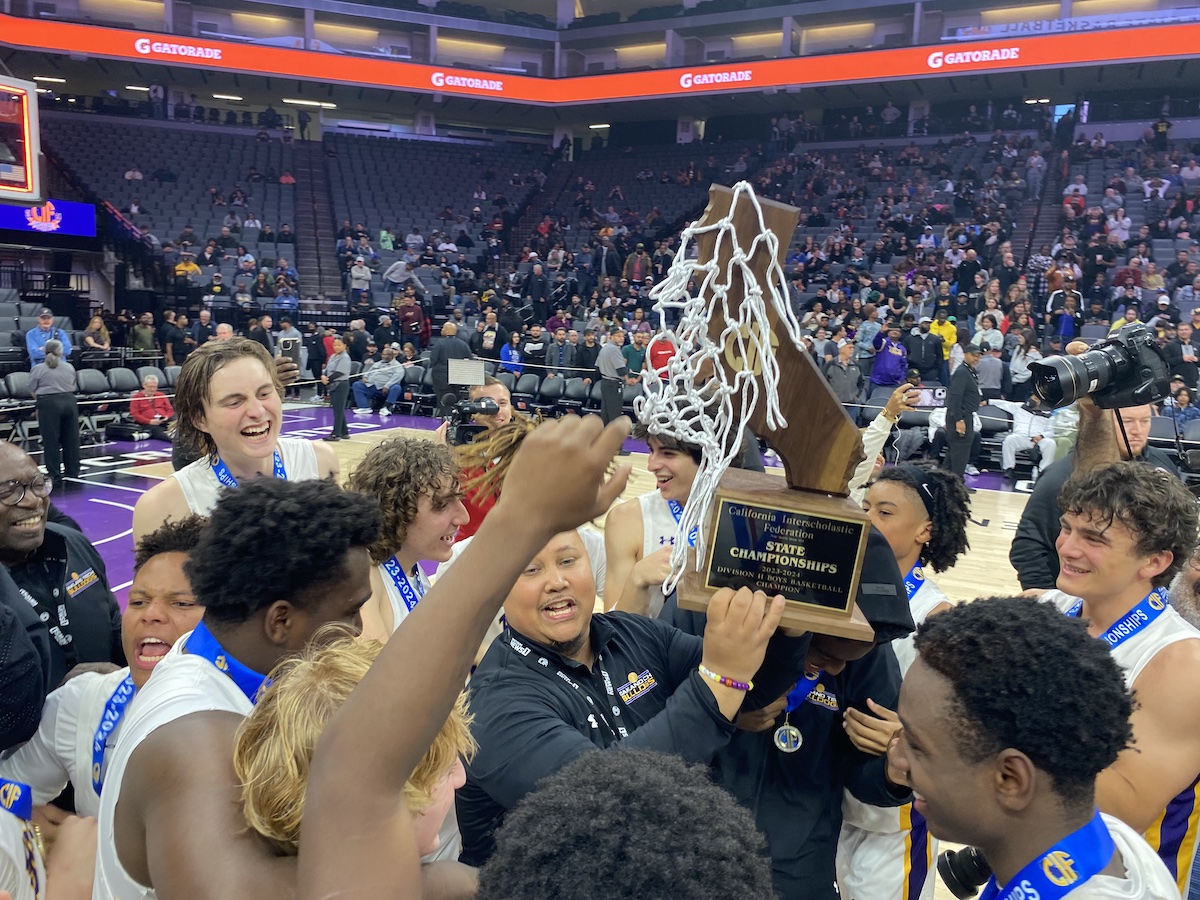 Basketball players and a coach hoist a trophy and cut net on the court after a game.